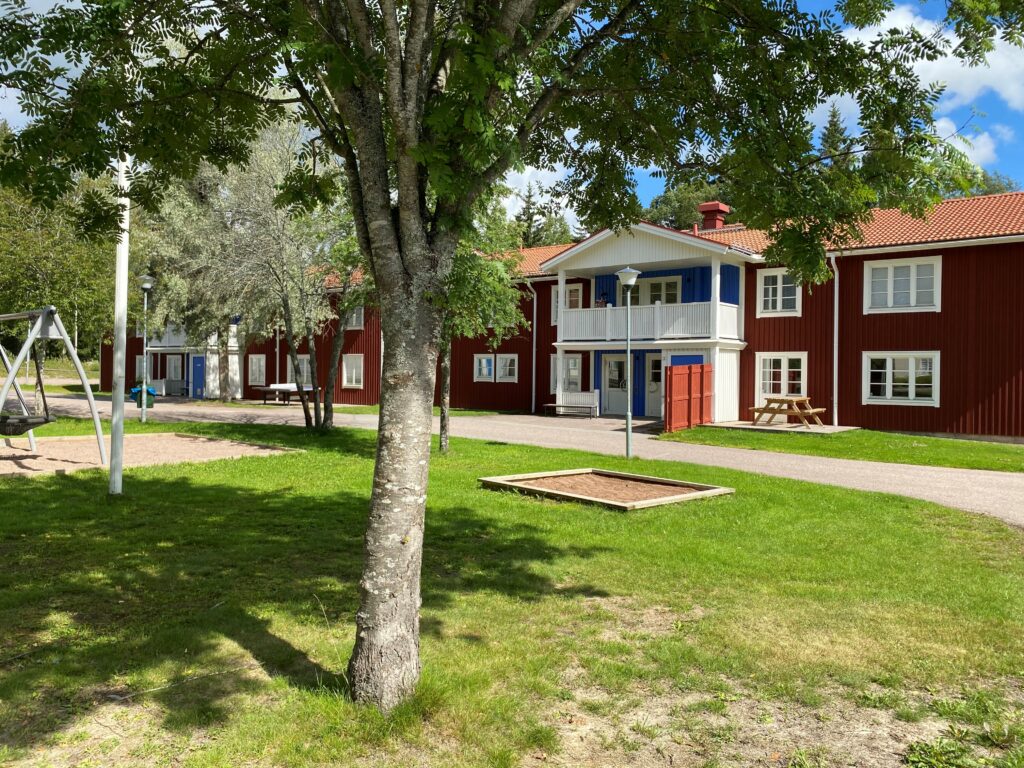 Röd och vitmålad skolbyggnad med träd på gården