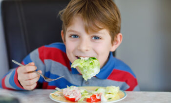 Glad pojke äter en god sallad med dressing