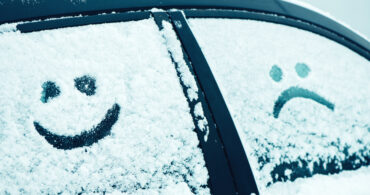 En glad och en sur gubbe ritad i snö på en bilruta.