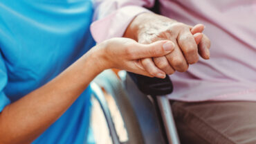 Vårdpersonal håller en äldres hand