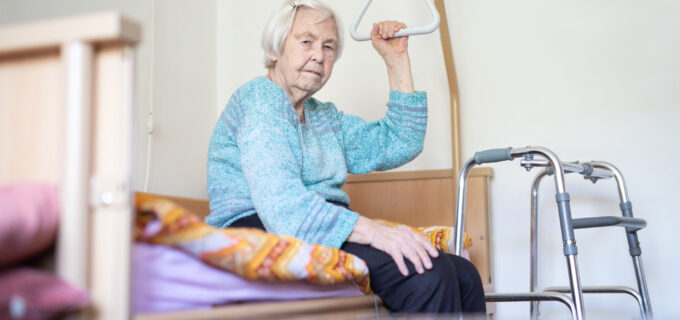 Äldre kvinna sittandes på en sjukhussäng.