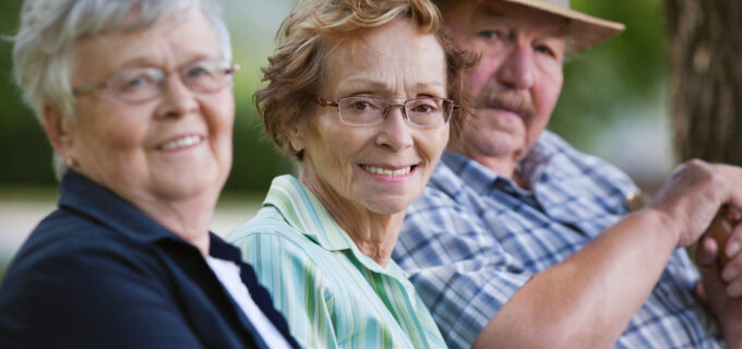 Tre pensionärer sitter tillsammans i en park.