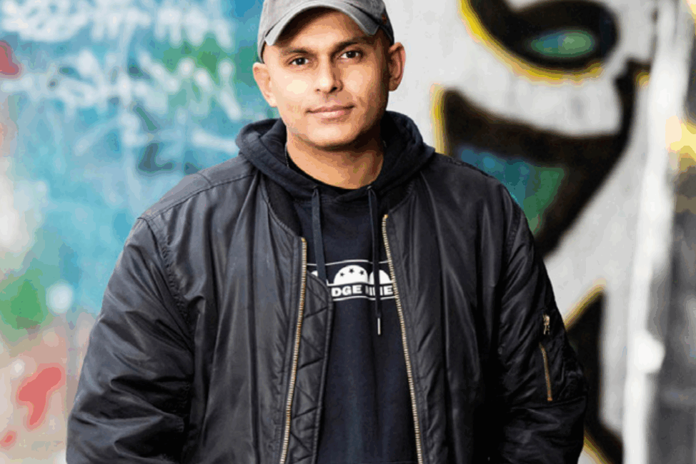 Kille med boberjacka och keps står framför en betongvägg med grafitti.