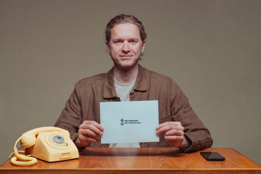 Man som sitter vid ett skrivbord och håller en lapp med texten Myndigheten för civilt försvar. 