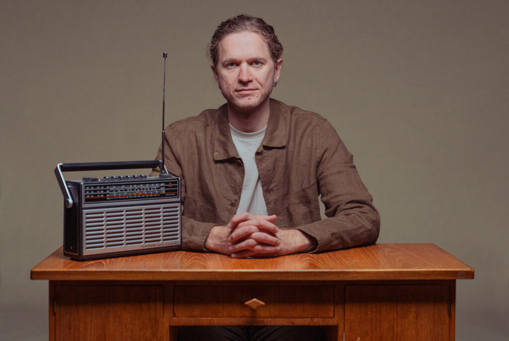 En man sitter vid ett skrivbord, en radio står på skrivbordet. 