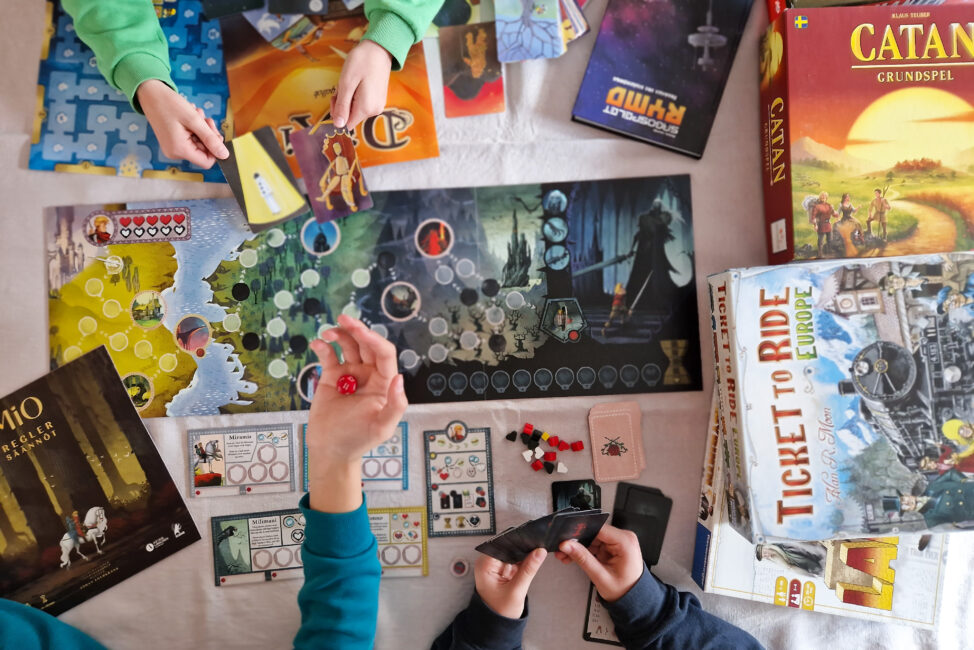 Brädspel utlagda på ett bord, tre par händer som spelar spel.