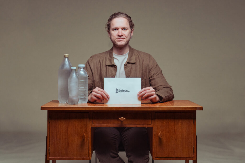 En man sitter vid ett skrivbord, vattenflaskor står på skrivbordet.