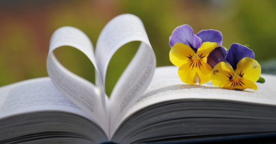 En uppslagen bok, varav två sidor formar ett hjärta. Till höger två blommor.