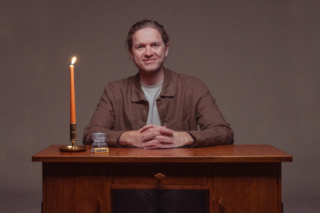 Man som sitter vid ett skrivbord. På skrivbordet står ett tänt stearinljus.