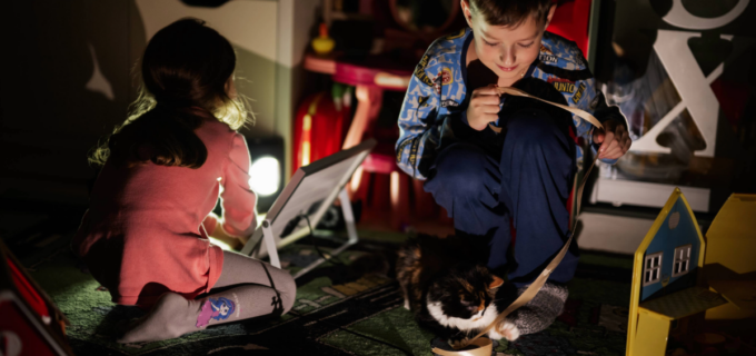Två barn som sitter i skenet av en batterilampa och leker.