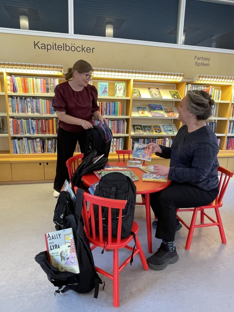 Två personer vid ett bord full med böcker. De packar böcker i ryggsäckar.