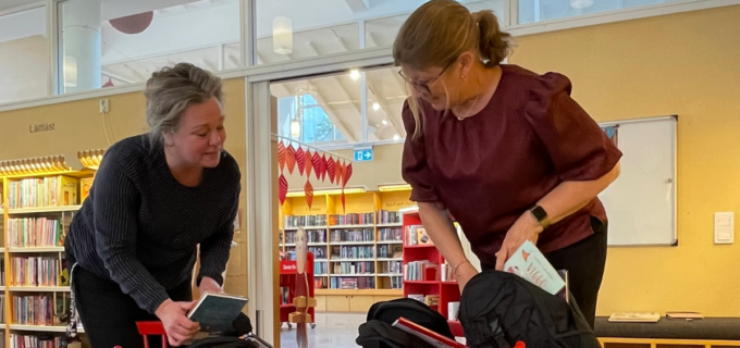 Två personer står vid ett bord full med böcker. De packar böcker i ryggsäckar.