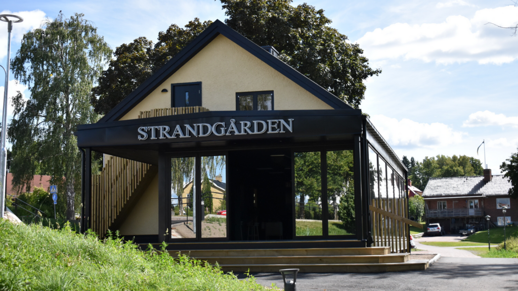 En ljusgul byggnad med ett stort öppningsbart glasparti, ovanför glaset står texten Strandgården.