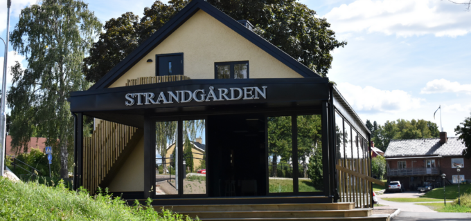 En ljusgul byggnad med ett stort öppningsbart glasparti, ovanför glaset står texten Strandgården.