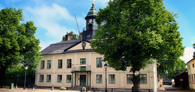 Rådhuset i Hedemora på sommaren, grönskande träd och blå himmel.