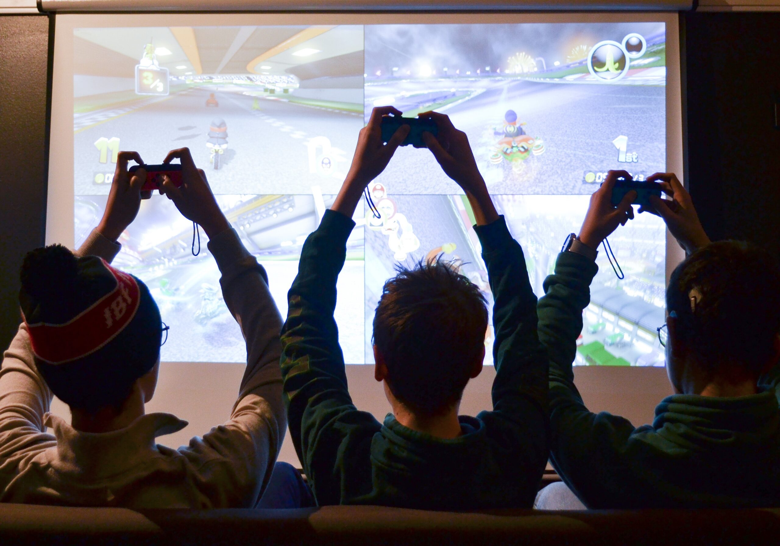 Tre personer som håller i en varsin spelkonsol framför en skärm.