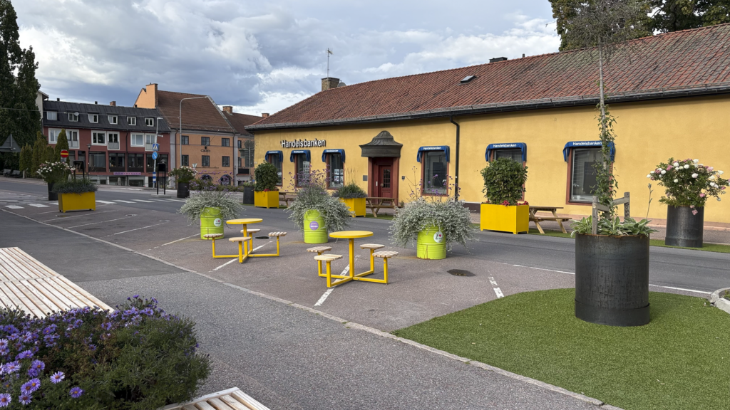Sommargata i Hedemora med gula bänkar, bord och planteringar.